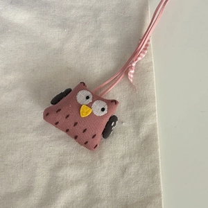 Détail du pendentif hibou en tissu rose avec noeud à carreaux sur lin beige doux