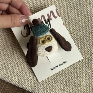 Detail of handmade plush dog hair clip with green hat and glasses on display card