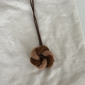 Détail d'un collier pendentif fleur en feutre fait main avec détails en coton et lin
