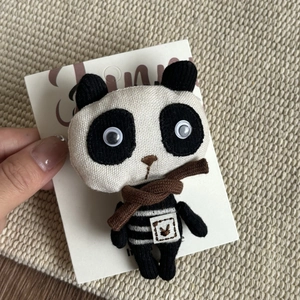 Detail of a handmade plush panda clip with cotton linen texture and striped sweater outfit