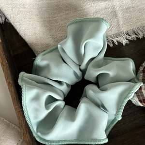 Pale mint green fabric scrunchie with refined edge stitching on a dark wooden tray
