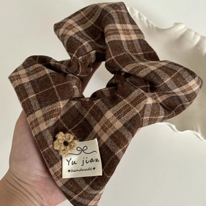Detail view of brown checkered scrunchie with handmade knit flower and woven label