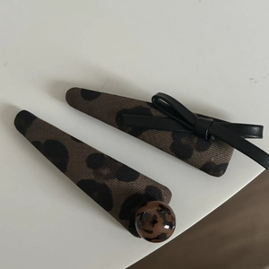 Détails de pinces à cheveux léopard avec nœud en cuir noir et boule ronde texturée