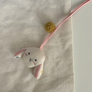 Détail d'un pendentif lapin en lin fait main avec cordon rose et pompon jaune gingembre