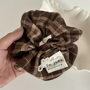 Detailed texture of brown plaid fabric scrunchie with a delicate white pearl bow accent