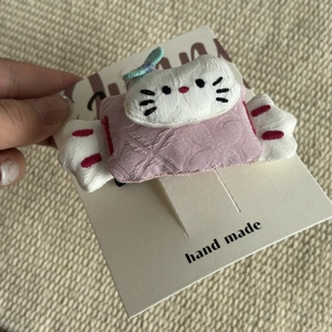 Detail of a handmade plush white cat hair clip with pink quilted fabric on card