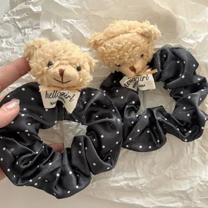 Détail d'un chouchou ours en peluche avec pois blancs sur tissu satiné noir