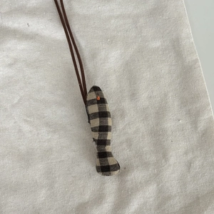 Détail d'un pendentif poisson en tissu à carreaux marron fait main sur fond de lin rustique