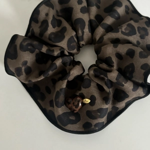 Détail d'un chouchou léopard avec texture satinée, breloque cœur et plaque Love