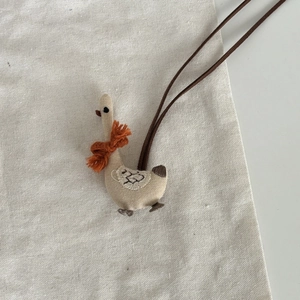 Détail d'un pendentif d'oie en lin fait main avec écharpe orange et cordons de suspension