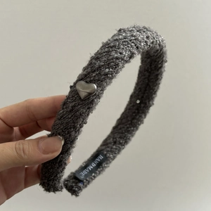 Détail d'un serre-tête gris en maille avec breloque cœur argentée et étiquette faite main