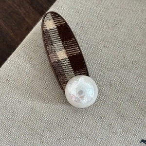 Détail d'une pince à cheveux à carreaux avec une grande perle sur un textile beige