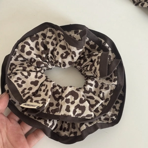 Detail view of a leopard print scrunchie with dark brown piping and a textile brand tag