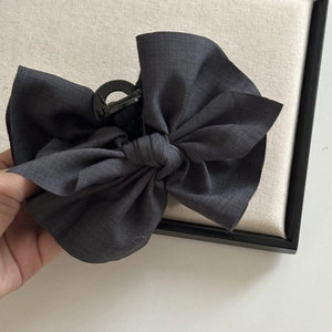 Détail du nœud en tissu gris foncé et de la pince crabe robuste pour la coiffure