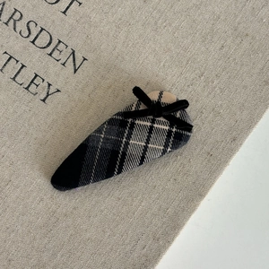 Preppy style grey plaid fabric hair clip with a small black velvet bow on burlap background