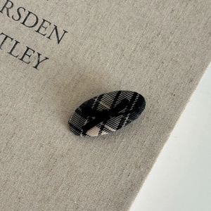 Detail view of oval fabric hair clip with black and white checkered pattern and a small bow