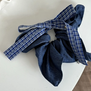 Detail of blue denim scrunchie with a plaid bow and a small golden metal accent