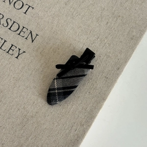 Detailed close-up of grey plaid fabric hair clip with a black ribbon bow on canvas