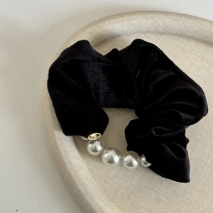 Elegant black velvet scrunchie with white pearls and gold charm on a cream display tray