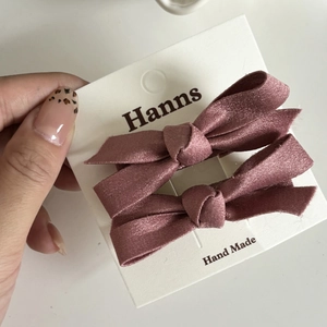 Détail de deux barrettes à nœuds en satin rose poudré sur une carte de présentation