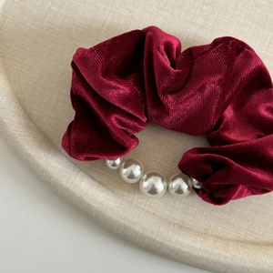 Elegant wine red velvet scrunchie with pearls on a textured beige display tray