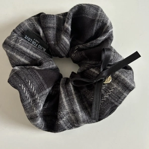 Detail of grey plaid scrunchie with a black silk bow and a small metal heart charm