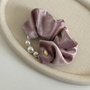 Close-up of pink velvet scrunchie featuring decorative white pearls and a gold tag