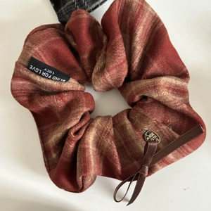 Detail of red plaid scrunchie with a ribbon bow and a gold heart-shaped metal pendant