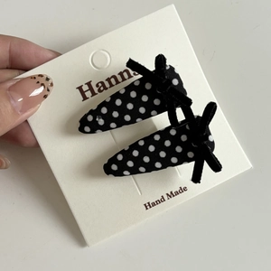 Détail de barrettes en tissu à pois avec nœuds en velours noir sur support en carton