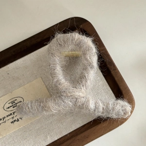 Détail de la pince à cheveux en peluche gris avoine sur un plateau en bois vintage