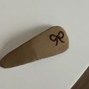 Close-up of khaki twill BB hair clip with detailed dark brown bow embroidery on top