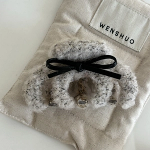 Elegant plush grey hair claw clip with black bow on beige canvas bag background