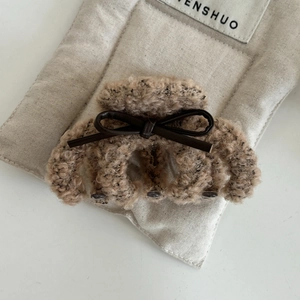 Brown plush hair claw clip with faux leather bow accent on a soft quilted surface