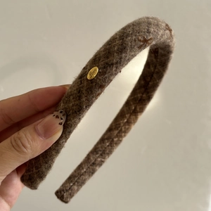 Detail of a brown tweed headband with a decorative golden metal Love logo charm