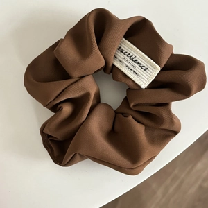 Detail view of brown pleated scrunchie with white woven excellence label and ribbed fabric