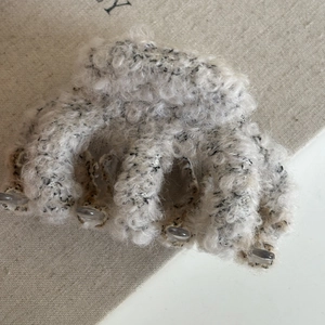 Detailed close-up of a plush beige hair claw clip with a cozy textured fabric finish