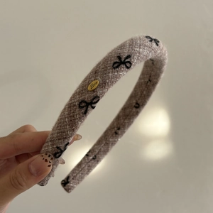 Detail of taupe flocked headband with black bow embroidery and gold Love metal tag