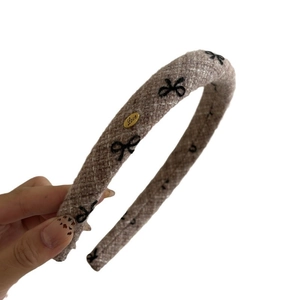 Thick tweed sponge headband with embroidered black bows and a gold logo tag