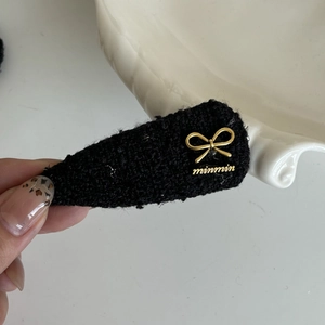 Detail of black tweed hair clip featuring an embossed golden metal bow ornament