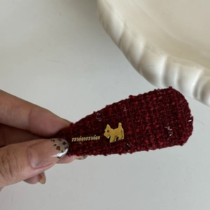 Elegant reddish-brown tweed hair clip with gold dog emblem and woven fabric texture