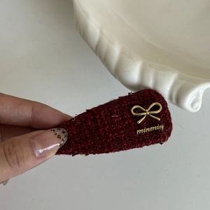 Detail of burgundy tweed hair clip with gold metal bow and minmin letter charms