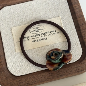 Dettaglio di un elastico vintage con una rosa in resina ambra e verde su base di legno