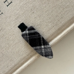 Détail de la pince à cheveux en tweed gris à carreaux avec base de bec de canard noire