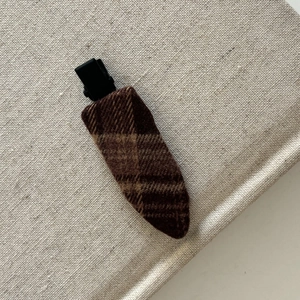 Vue détaillée de la pince à cheveux à carreaux café avec tissu en laine texturé