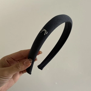 Détail d'un serre-tête en tissu gris rembourré avec un petit nœud en métal argenté