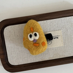 Barrette en feutre de laine jaune avec visage de dessin animé sur fond bois et lin