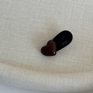 Close-up of heart-shaped dark brown hair clip on textured beige fabric background