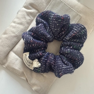 Détail du chouchou en tricot bleu foncé avec points colorés et breloque en cœur argenté