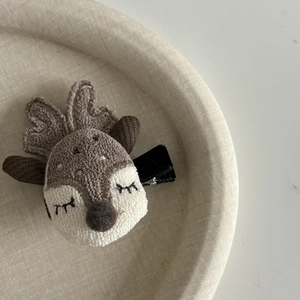 Détail d'une pince à cheveux renne en peluche avec texture 3D sur fond beige texturé