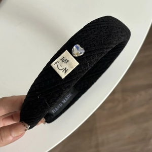 Détail d'un serre-tête en tissu noir texturé avec cœur en cristal et étiquette fun